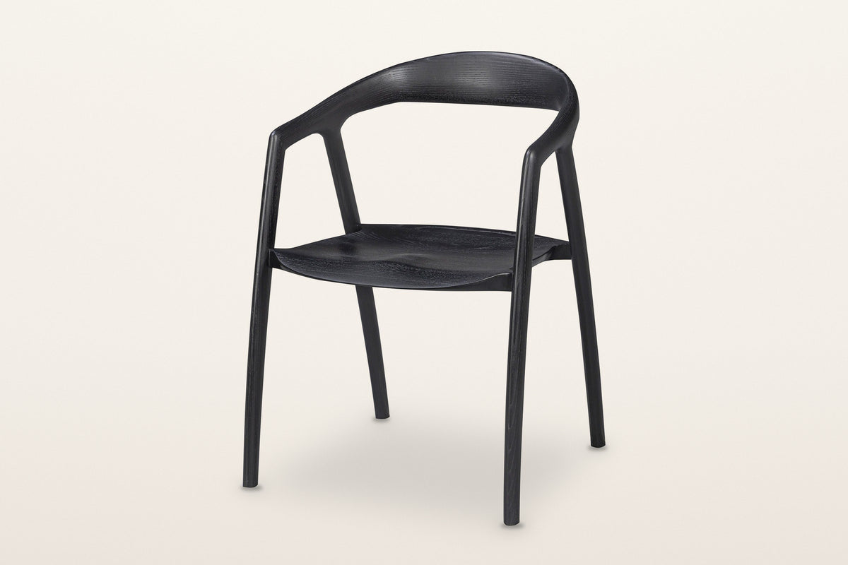 Pollica solid ash dining armchair in Black, three-quarter view on a warm white studio backdrop