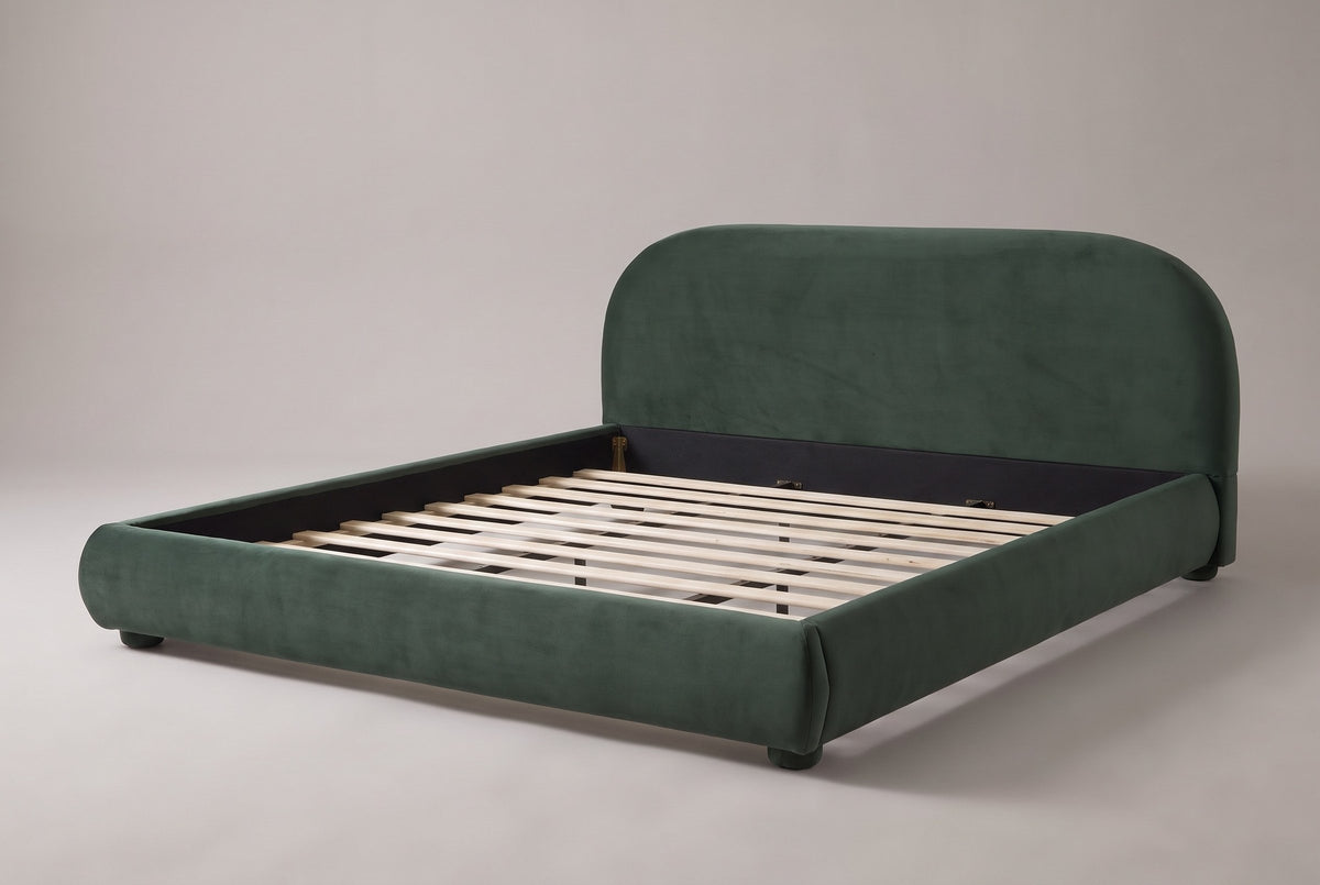 Pollutri upholstered bed in dark green velvet, three-quarter view on a warm grey studio backdrop