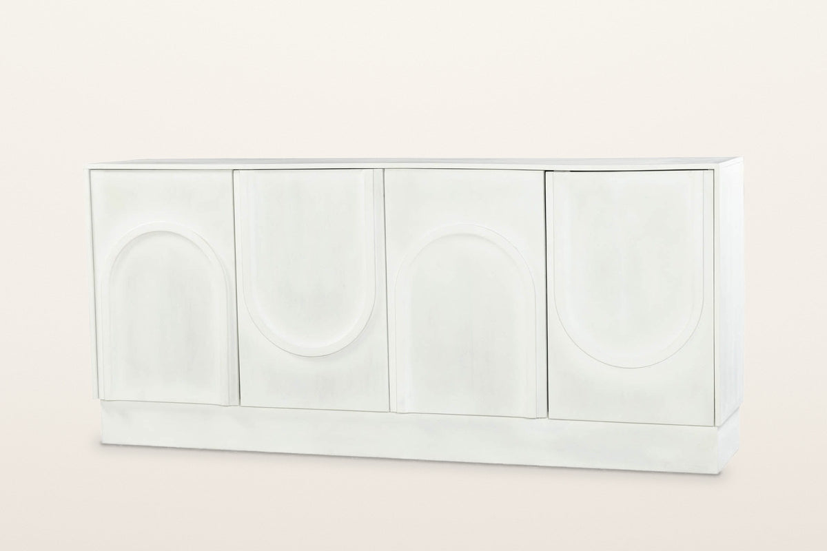 Pragelato 76 in sideboard in white-washed mango wood: four doors with raised arches that alternate up and down, no handles, on a deep plinth, three-quarter view on a warm white studio backdrop