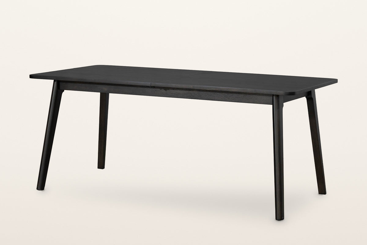 Prescott round-leg extension dining table in Antique Black, closed to 70 in, three-quarter view on a warm white studio backdrop