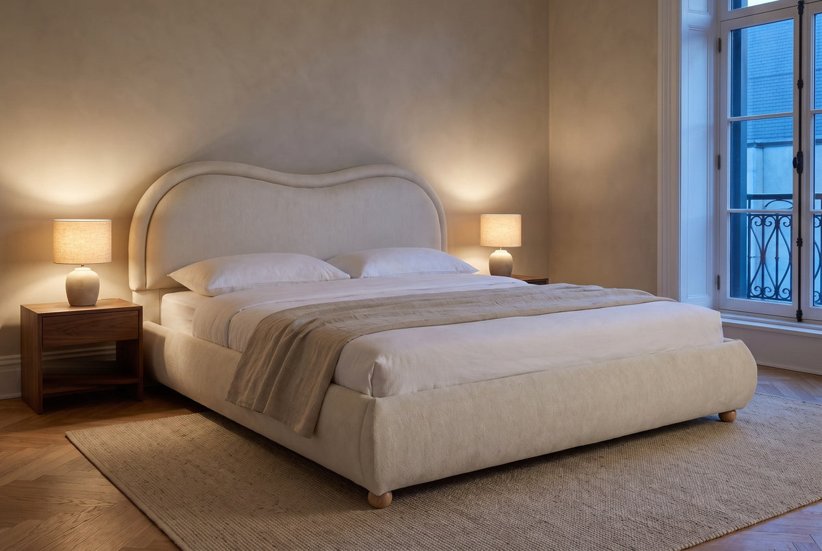Recanati cloud bed in a limewashed bedroom at dusk, two lamps lit on walnut nightstands, a wrought-iron balcony outside