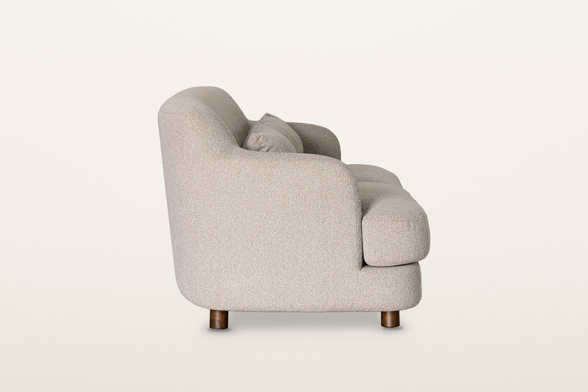 Ripatransone sofa in Beige, side view on a warm white studio backdrop: the back curves down into the arm and the seat cushion