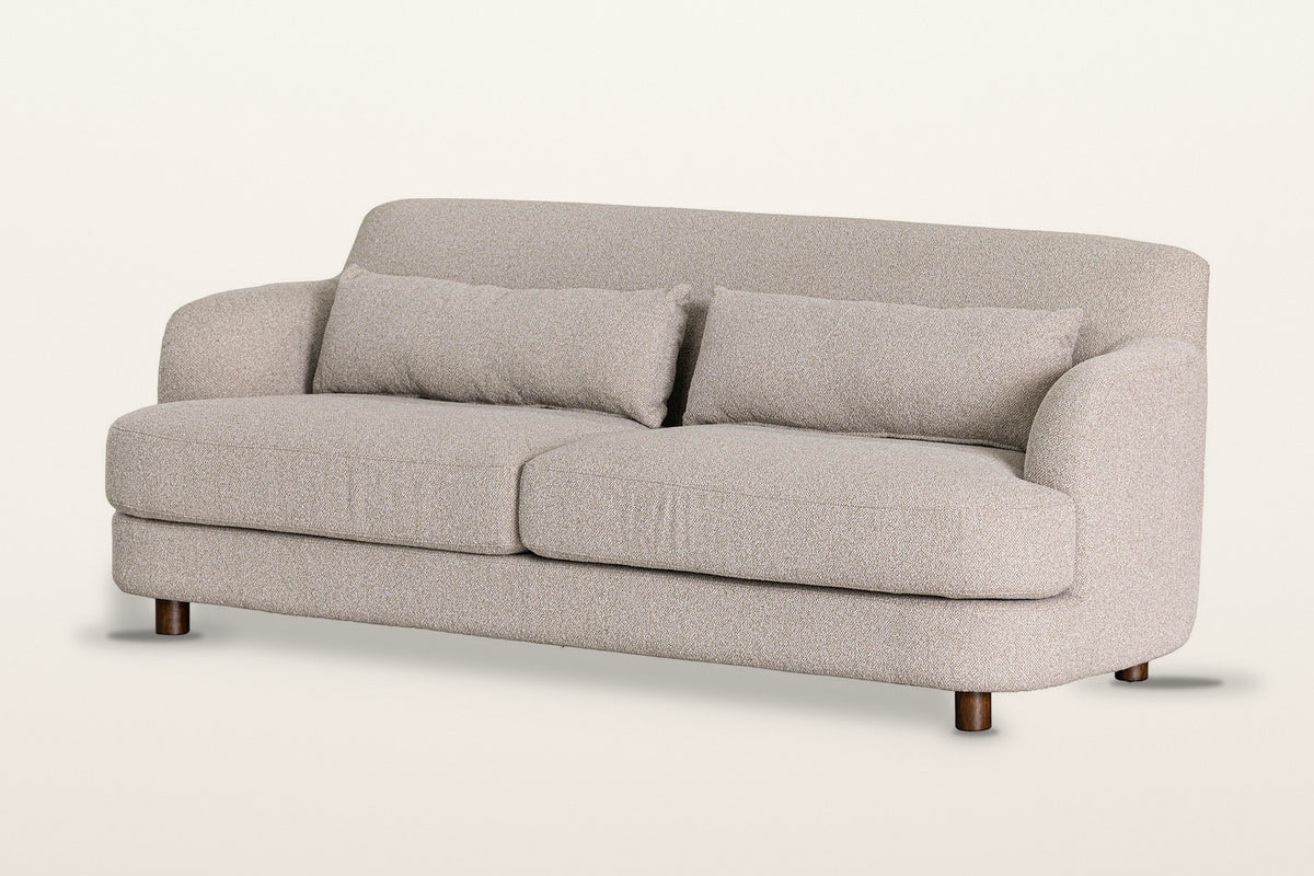 Ripatransone sofa in Beige, three-quarter view on a warm white studio backdrop: a tight curved back that sweeps into low roun