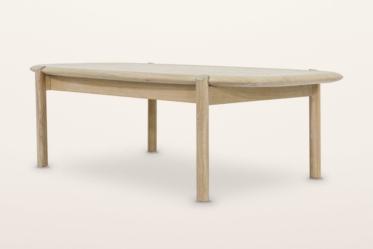 Rivello coffee table in Light Oak, low three-quarter view on a warm white studio backdrop: four round legs and the apron