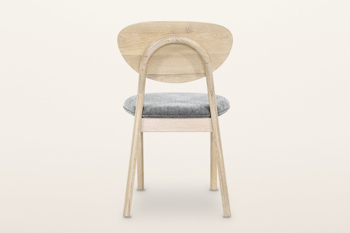 Rivello dining chair in Light Oak from behind on a warm white studio backdrop: the round rear legs bend into one oak arch beh