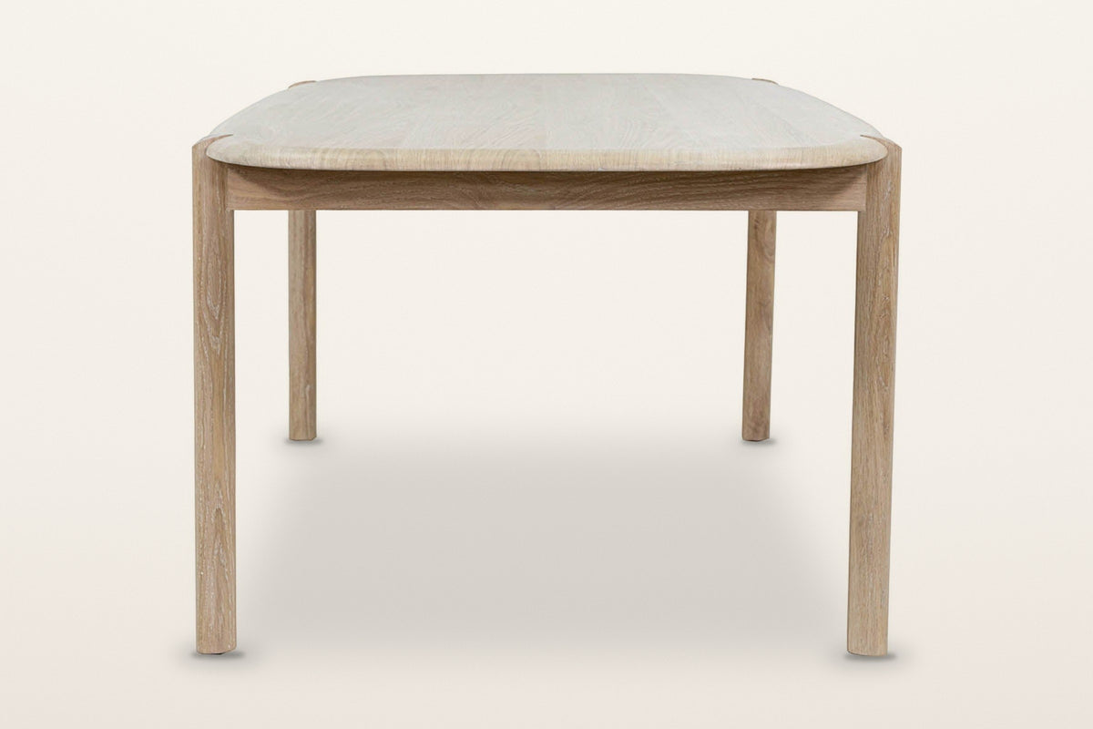 End view of the Rivello dining table in Light Oak on a warm white studio backdrop: the rounded end over round legs