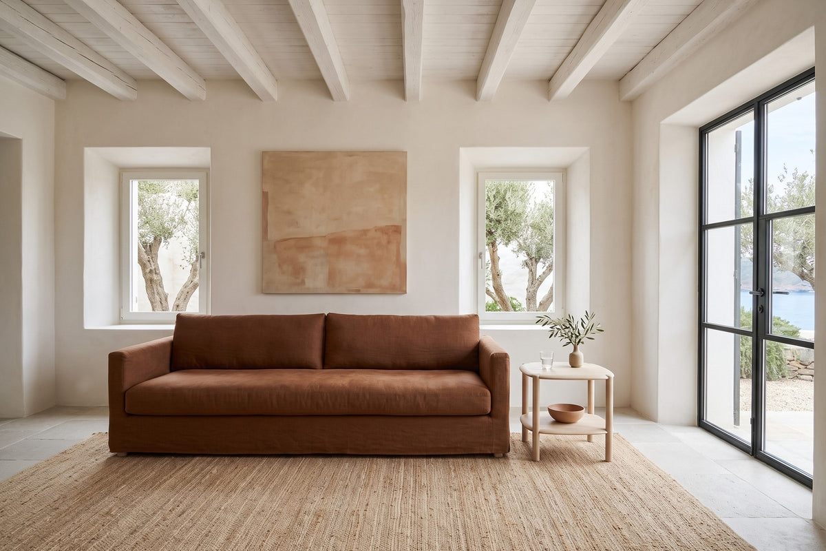 Front view of the Rivello side table in Light Oak at the arm of a rust linen sofa in a whitewashed house by the sea