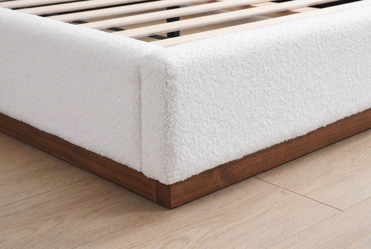 Close-up of the foot corner of the Roccascalegna bed: the white boucle rail on its recessed walnut plinth