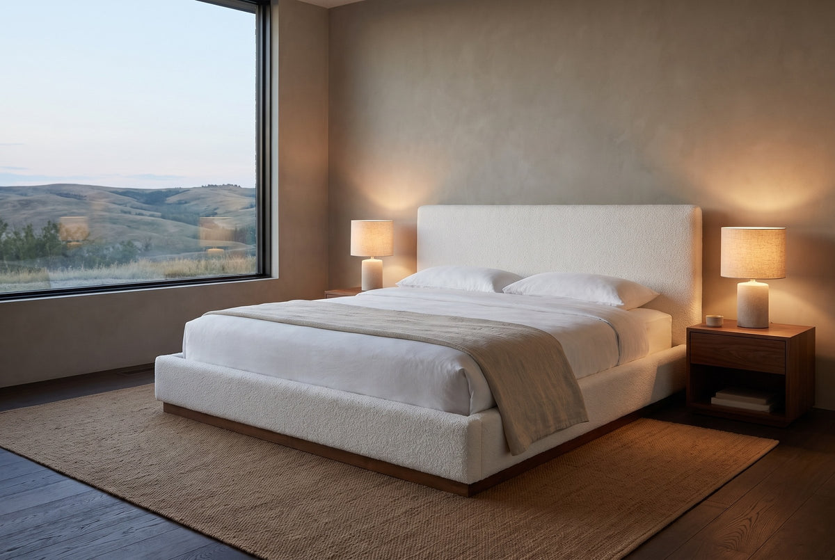 Roccascalegna boucle bed in a plaster bedroom at dusk, two lamps lit, with a picture window onto rolling foothills
