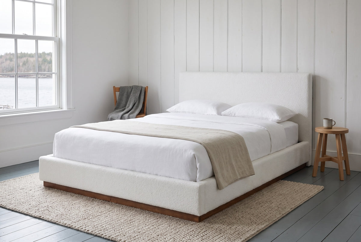 Roccascalegna boucle bed in a white panelled bedroom with grey-blue floorboards and a window onto the harbour