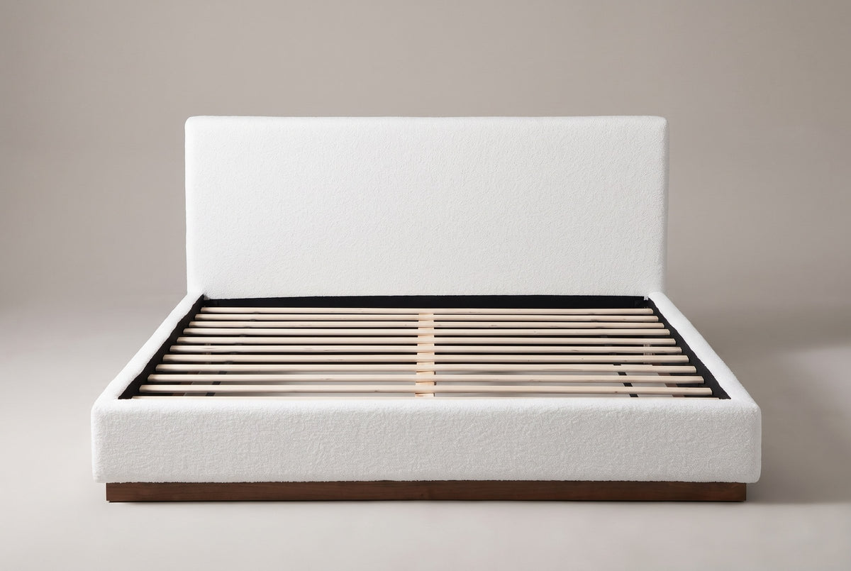 Roccascalegna boucle bed seen straight on from the foot: plain headboard, wood slats and a recessed walnut plinth