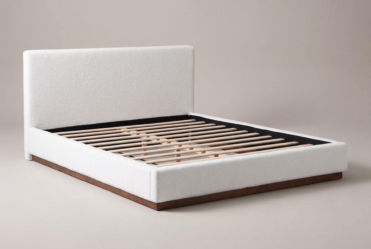 Roccascalegna boucle platform bed in white, three-quarter view on a warm grey studio backdrop, with its walnut plinth