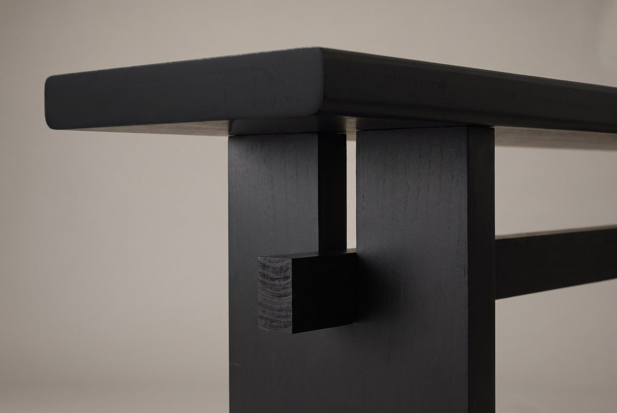 Close-up of a black slab leg: the slot under the top, the recessed post and the square stretcher end showing its end grain