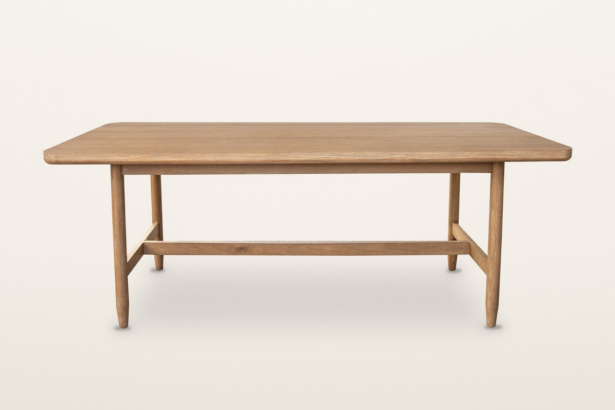 Sarnano dining table in Sand, straight front view on a warm white studio backdrop: a long top with rounded corners on four ta