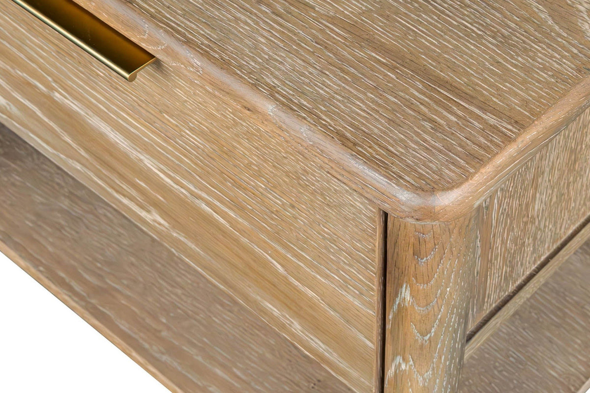 Close-up of the Sarnano top's rounded corner over a round oak leg, the end of the brass pull on the drawer at the left