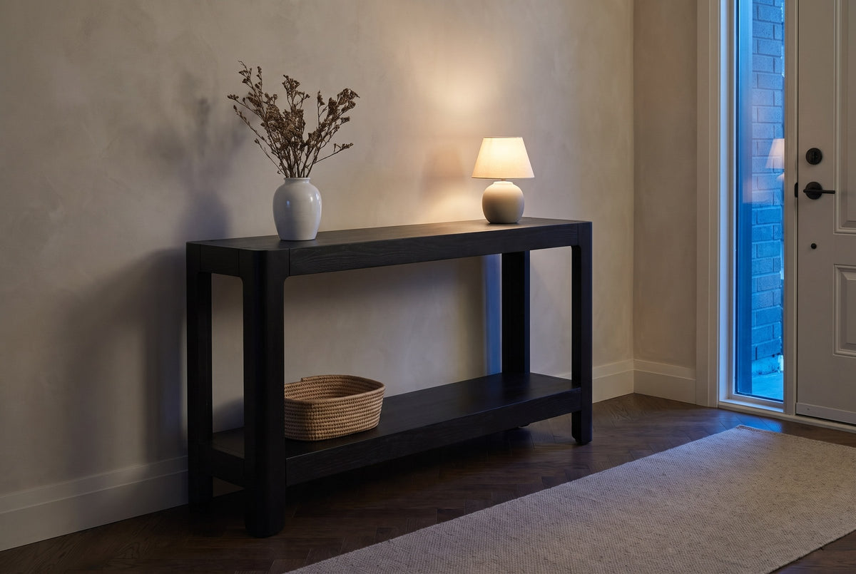 Sarnico console table in a townhouse entry at dusk, a small lamp lit and a woven basket on the lower shelf