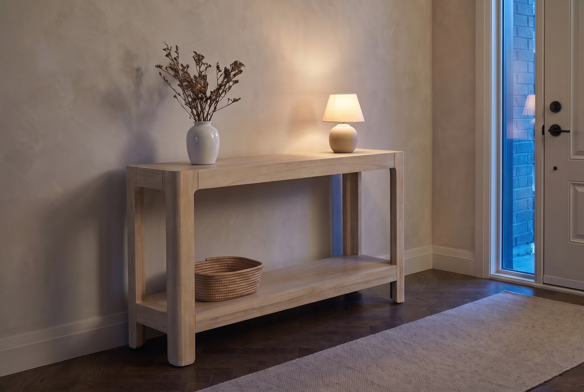 Sarnico console table in natural in a townhouse entry at dusk, a small lamp lit and a woven basket on the lower shelf