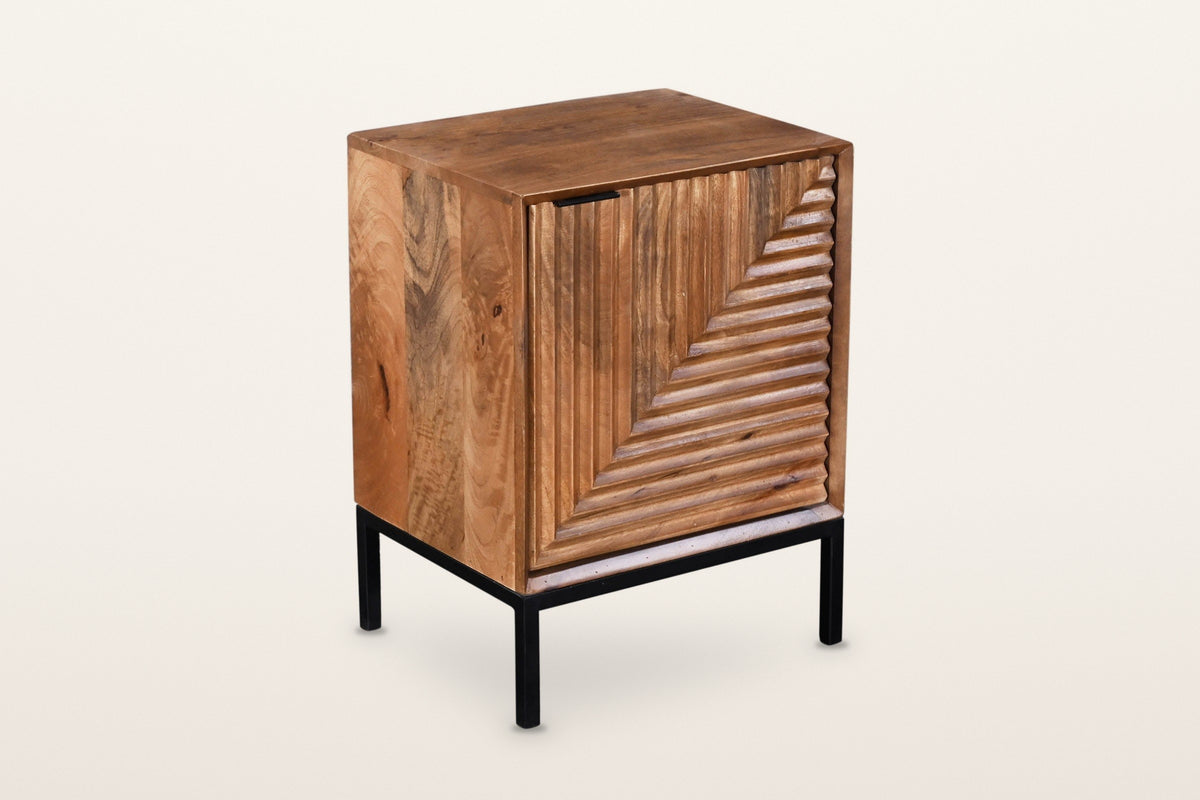 Sarteano nightstand in Pecan mango wood, three-quarter view on a warm white studio backdrop: one door carved with flutes that