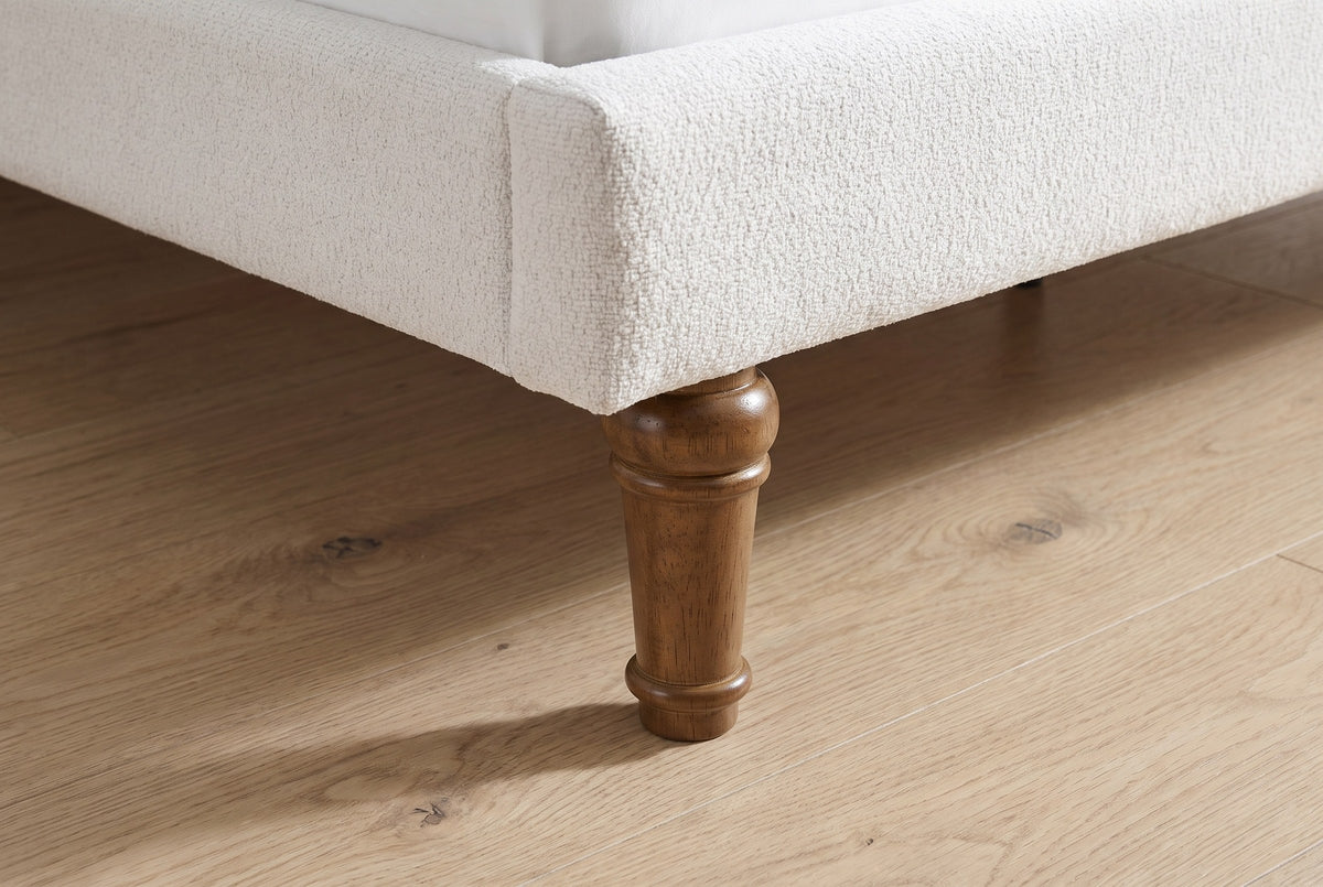 Close-up of a turned walnut-stained wood leg under the upholstered foot rail