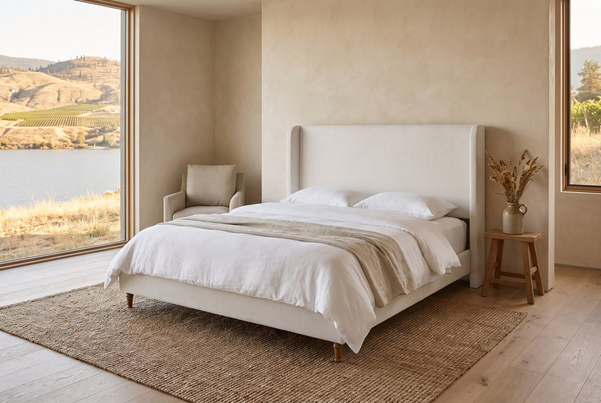 Sarzana wingback bed in a lake house bedroom with limewashed walls, a jute rug and vineyard hills outside