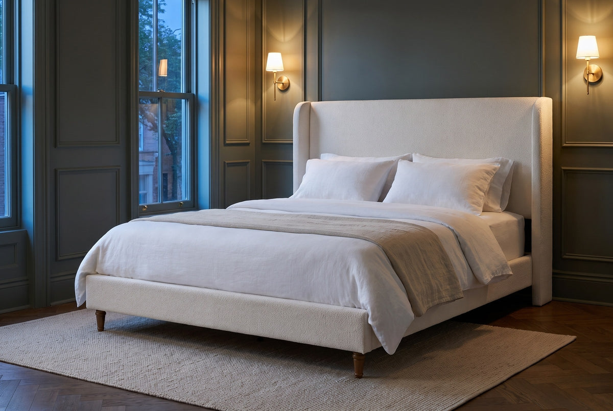 Sarzana wingback bed in a panelled bedroom at dusk, brass sconces lit on dark green walls