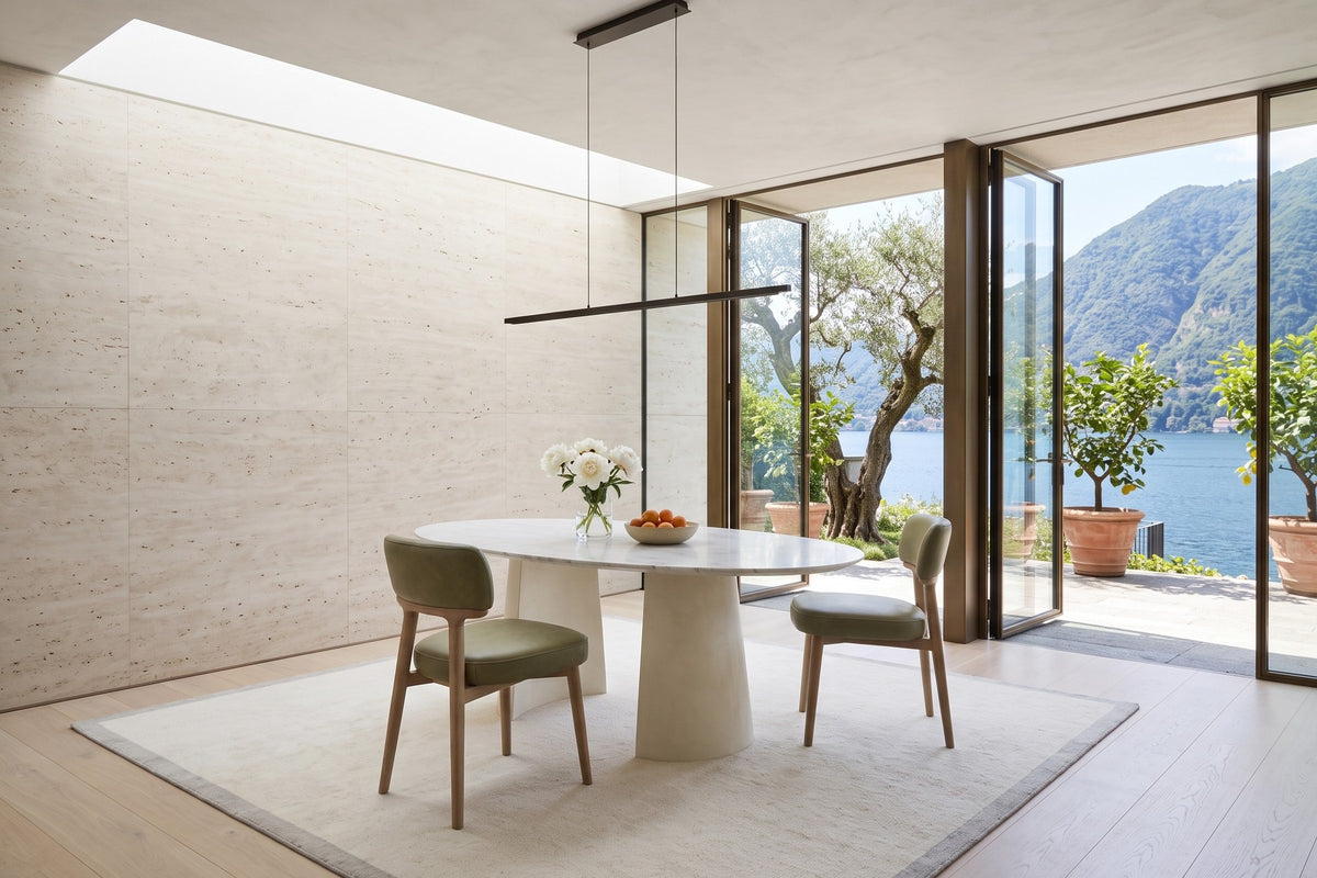 Two Savoca dining chairs in Sage Green leather at an oval white marble table in a villa on Lake Orta, with travertine walls
