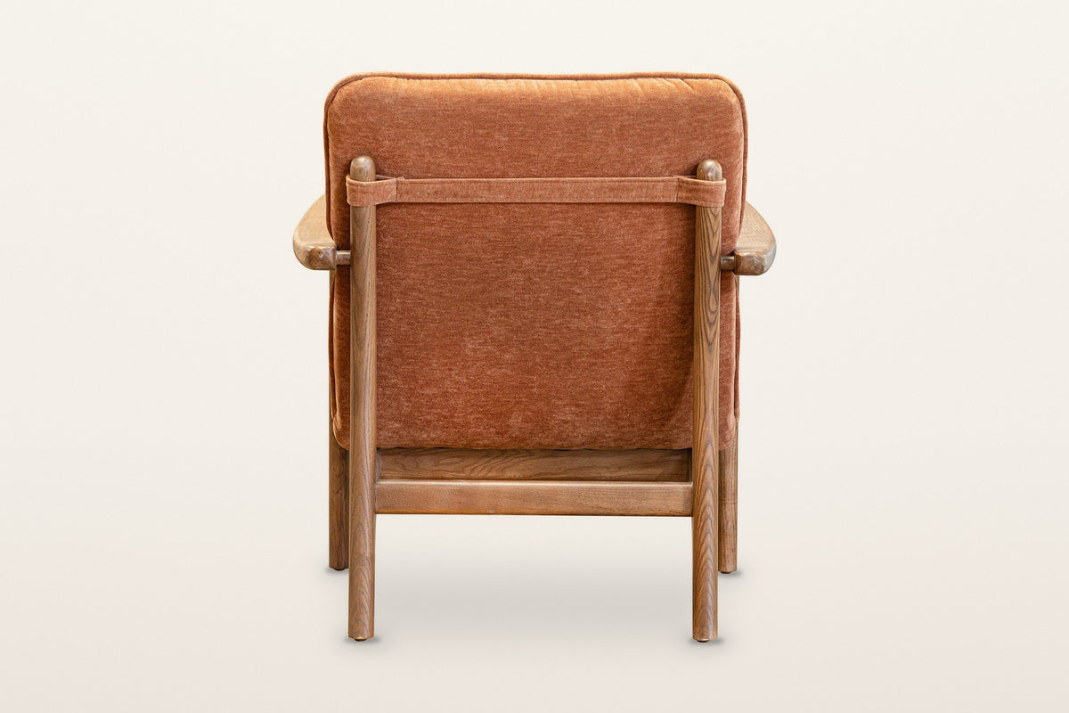 Back of the Servigliano accent chair in Rust on a warm white studio backdrop: a fabric strap between the two back posts holds