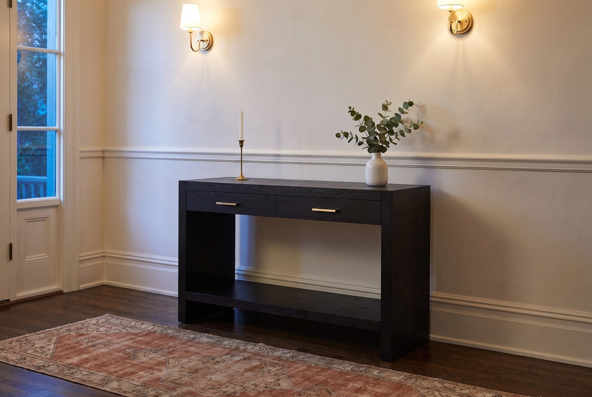 Sibari console table in a plaster entry hall in Victoria at dusk, brass sconces lit, a candlestick and eucalyptus on top