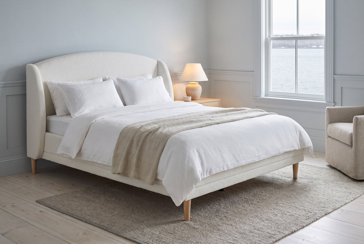 Sirmione boucle wingback bed in a blue-grey bedroom with a window over the harbour and a lit lamp