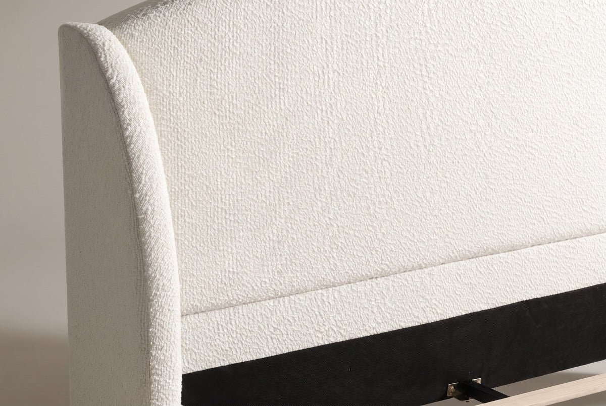 Close-up of a rounded boucle wing beside the plain arched headboard