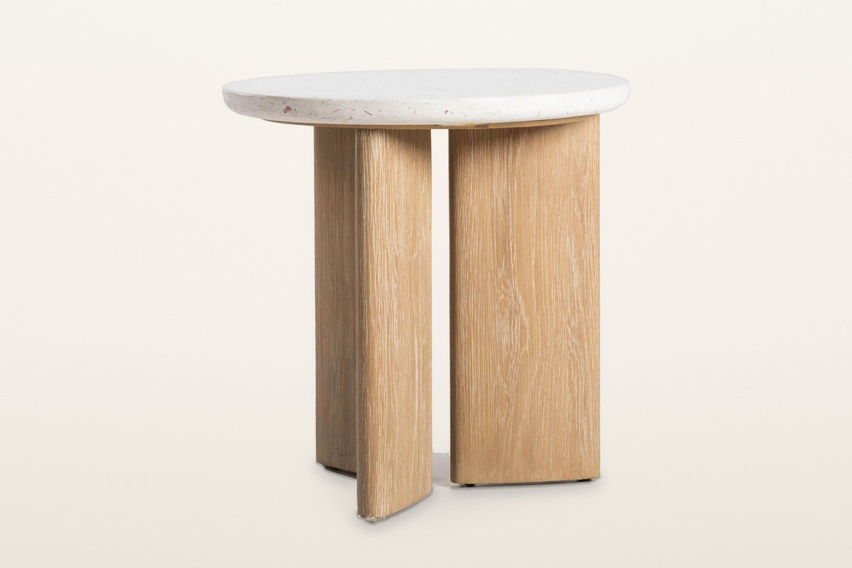 Sorano side table at eye level on a warm white studio backdrop: the round terrazzo top and the oak slab legs with a gap betwe