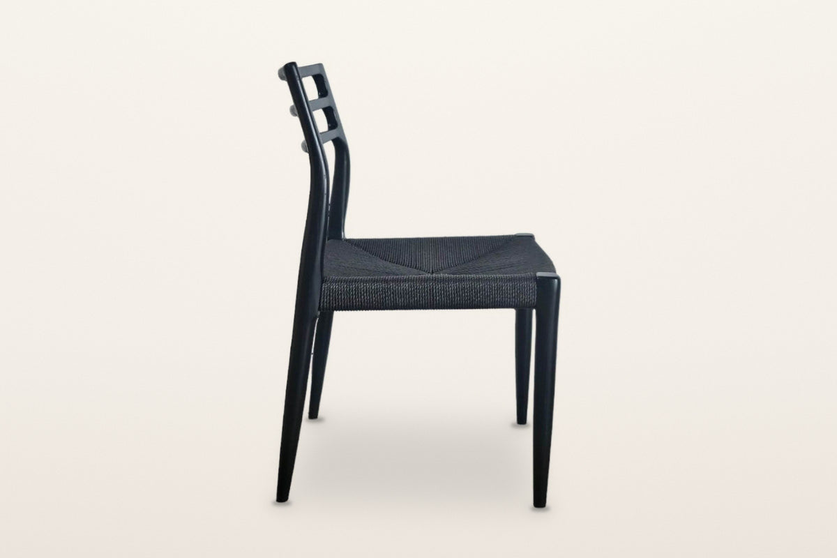 Sperlinga dining chair in black, side view on a warm white studio backdrop: the rear leg runs up into the curved back post