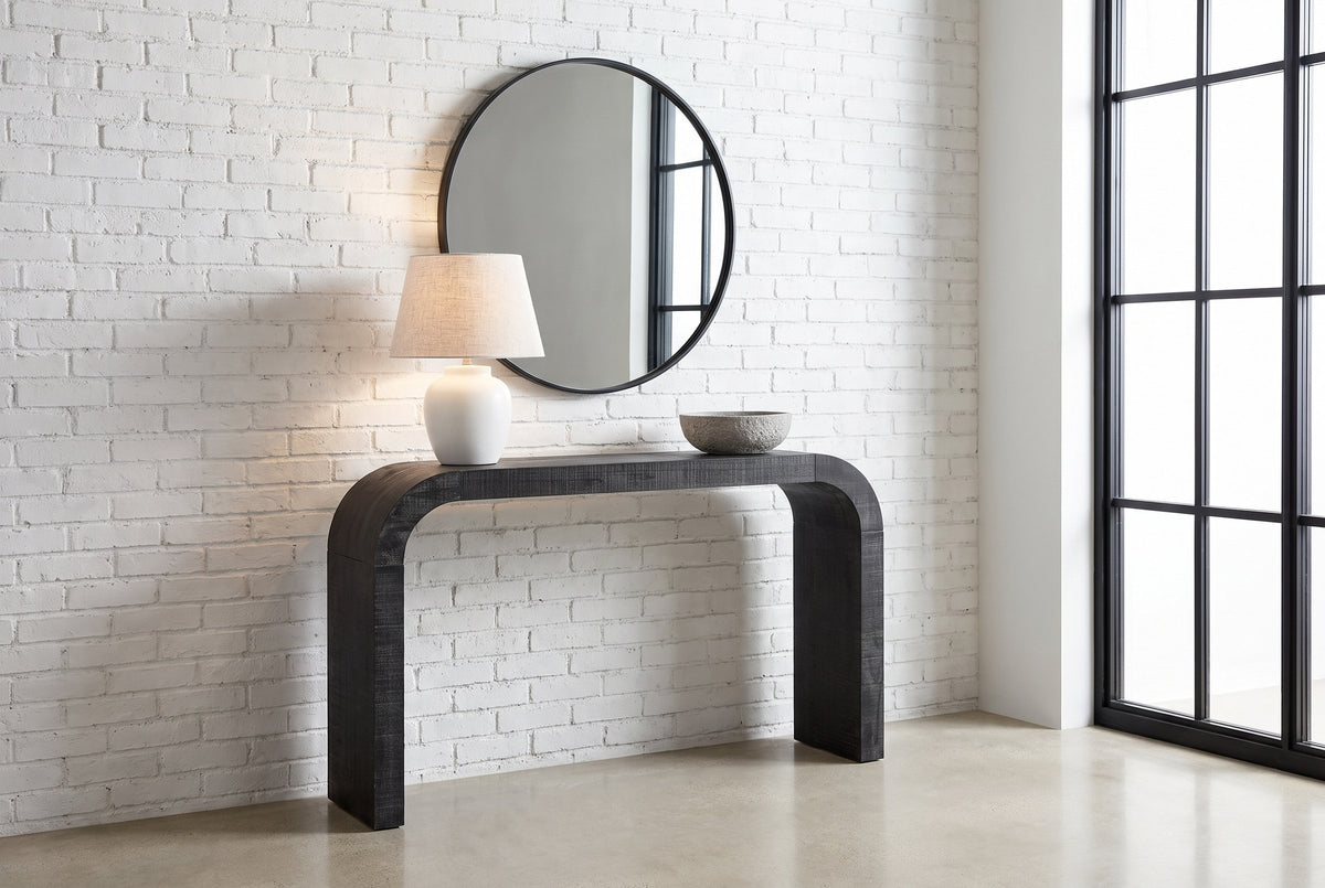 Tarvisio console table in black in a Montreal loft entry, a white lamp and a stone bowl on top, a round mirror above