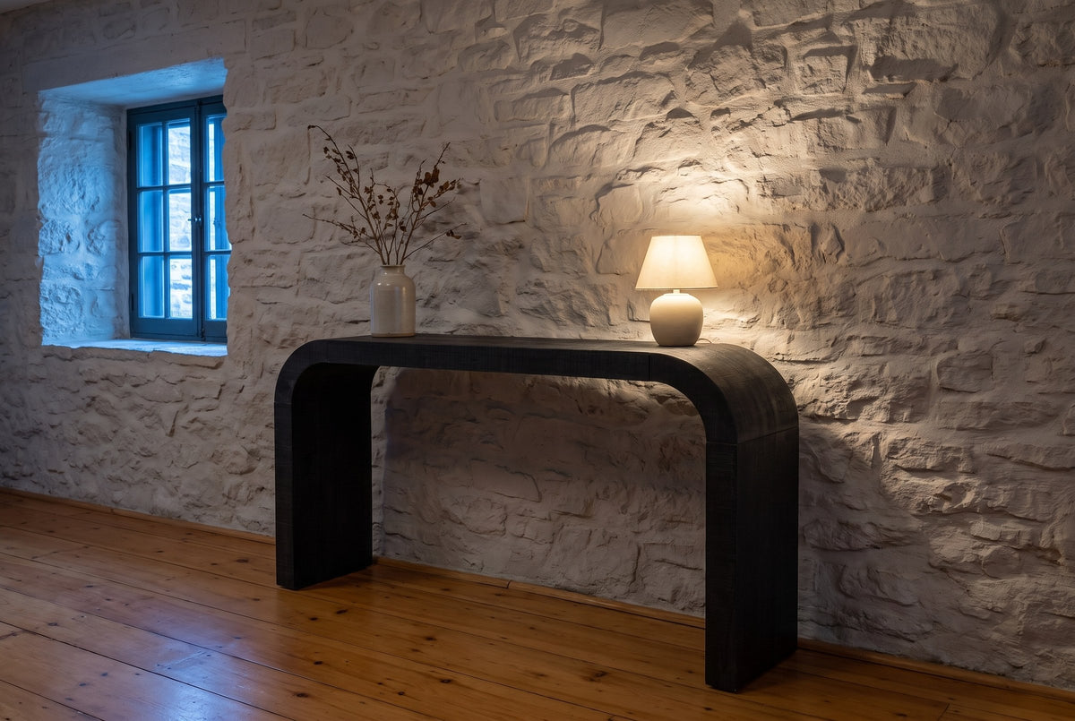 Tarvisio console table against a limewashed stone wall in a Quebec City hall at dusk, a small lamp lit