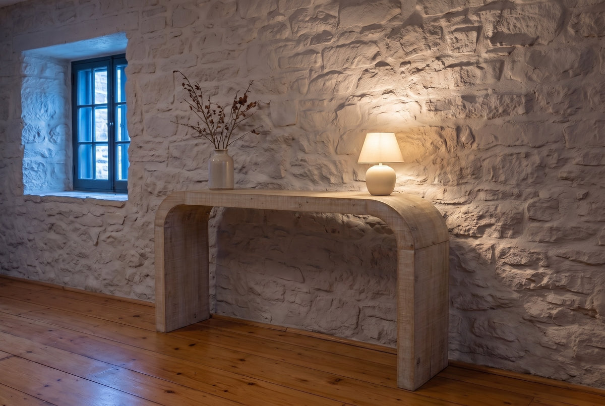 Tarvisio console table in natural against a limewashed stone wall in a Quebec City hall at dusk, a small lamp lit