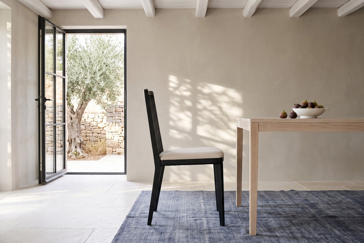 A Teggiano dining chair in Black in side profile at a bleached-oak table in a stone house in Kardamyli