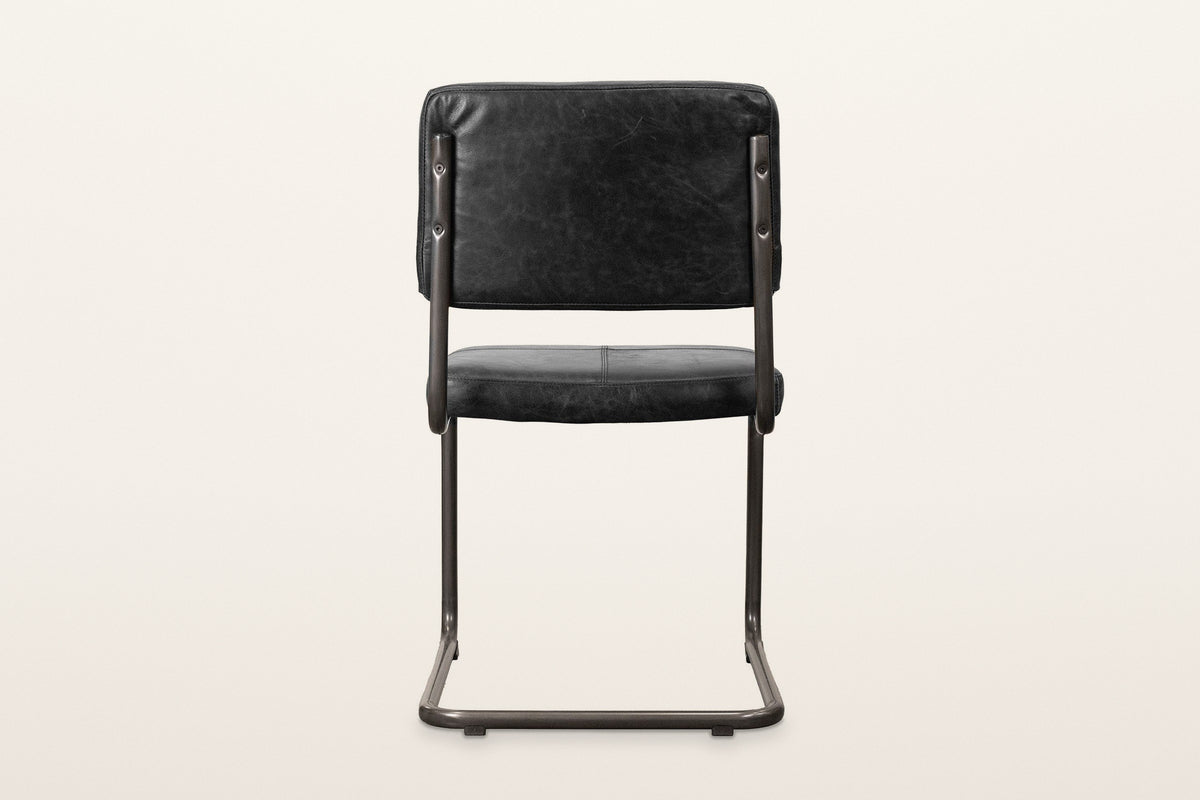 Back of the Tenno dining chair in Black on a warm white studio backdrop: the plain back of the cushion and the two posts