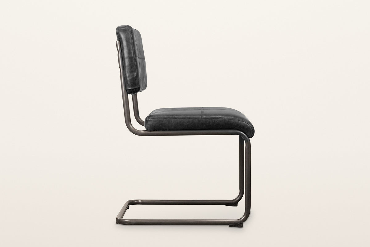 Tenno dining chair in Black, side view on a warm white studio backdrop: one bent tube from the back post to the floor and bac