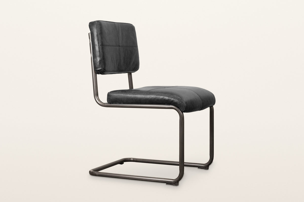 Tenno dining chair in Black, three-quarter view on a warm white studio backdrop: black leather cushions on a bent iron tube f
