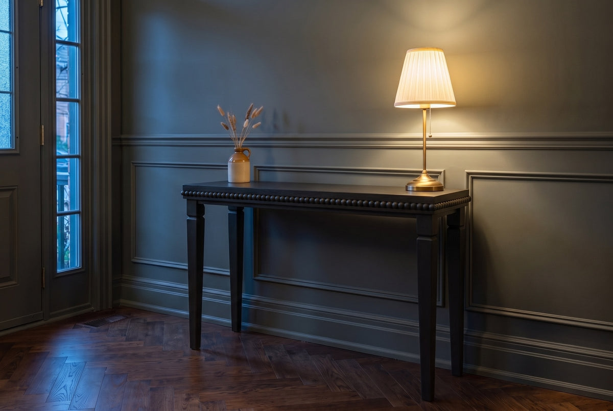 Treviso console table in Black in a green-grey panelled Toronto front hall in the evening, a brass lamp lit at one end