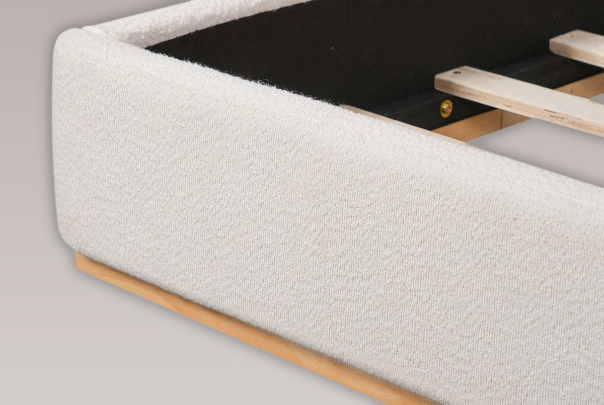 Close-up of the foot corner of the Varenna bed: the rounded boucle rail on its recessed natural rubberwood plinth