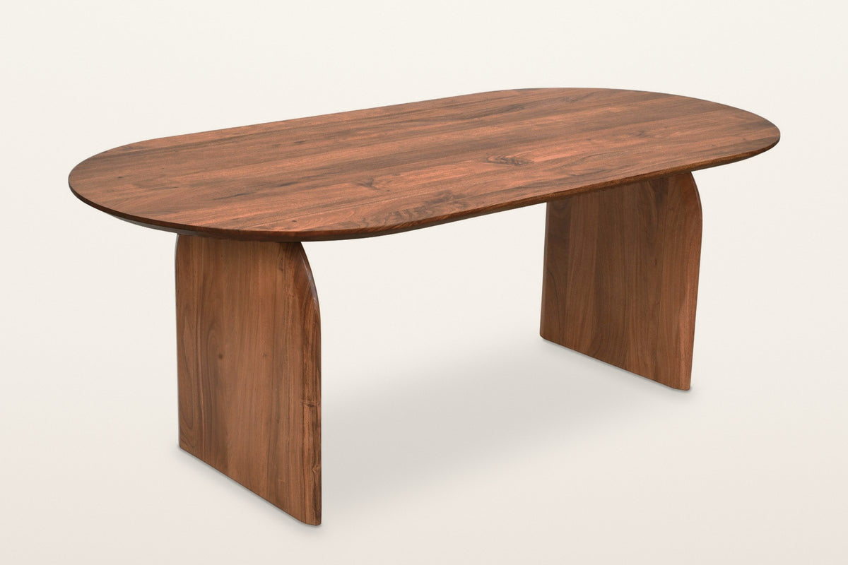 Visso dining table in Pecan, three-quarter view on a warm white studio backdrop: a long top with round ends on two arched pan