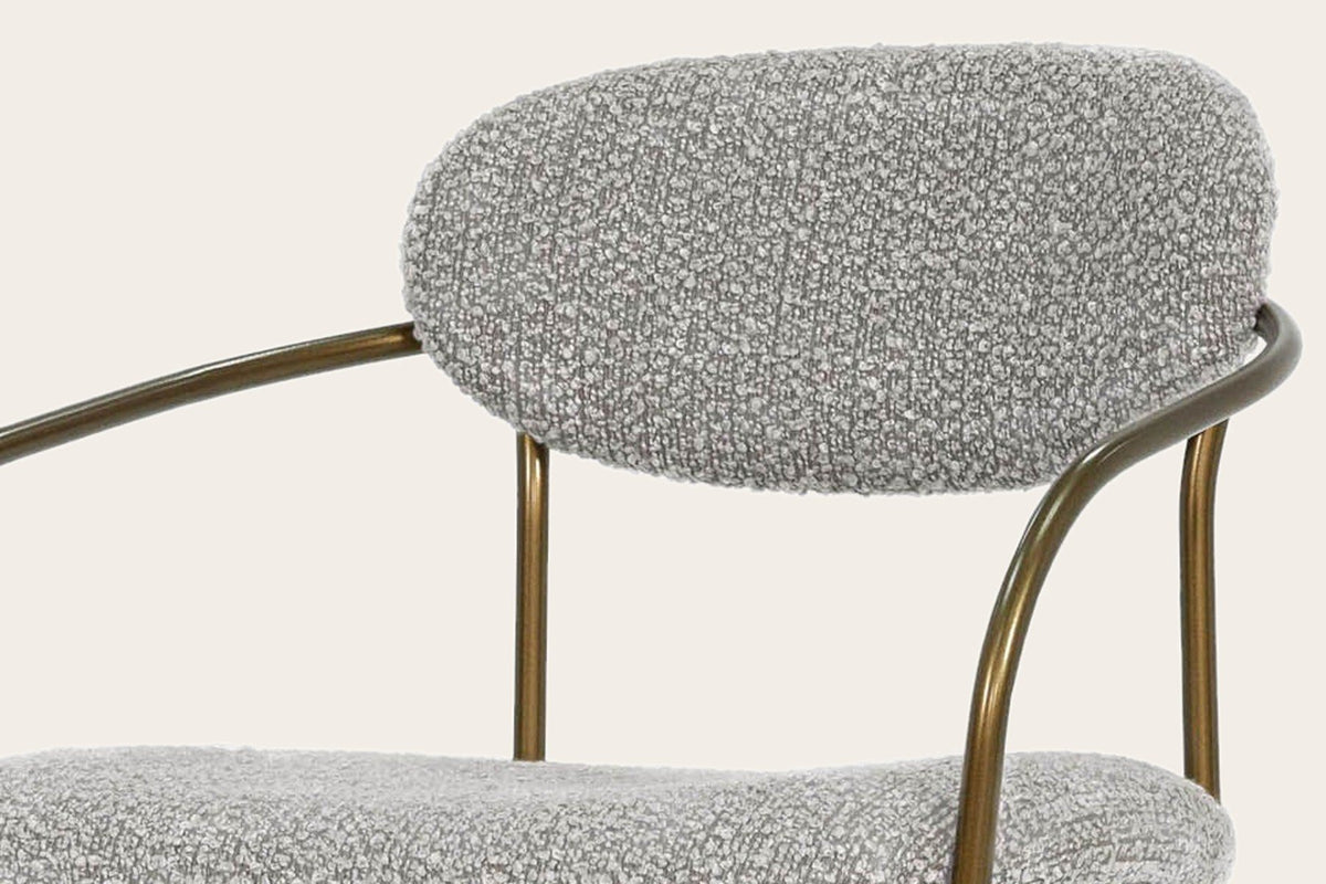 Close-up of the Vitorchiano chair: the Pearl Grey bouclé back pad, the antique bronze hoop behind it and the bent arm tube