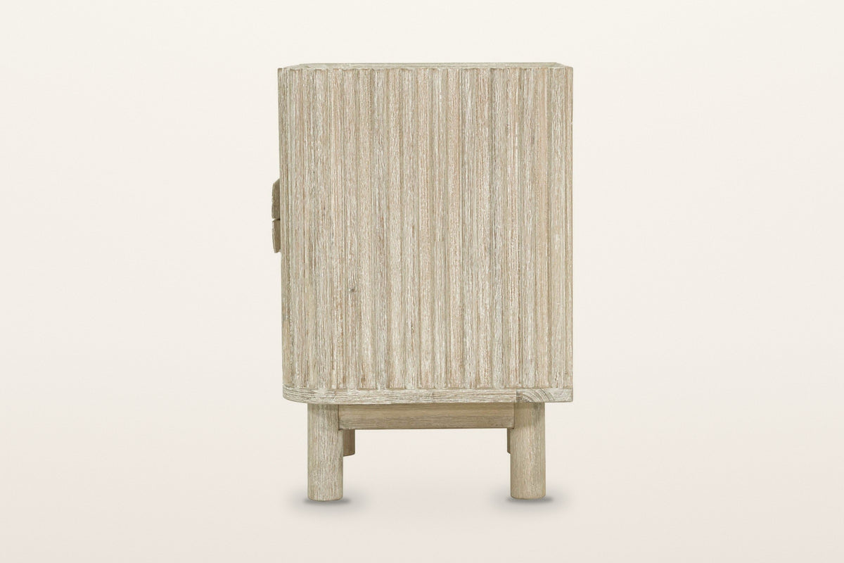 Side view of the Vitorchiano nightstand in Natural White Wash on a warm white studio backdrop: the reeded side over the plint