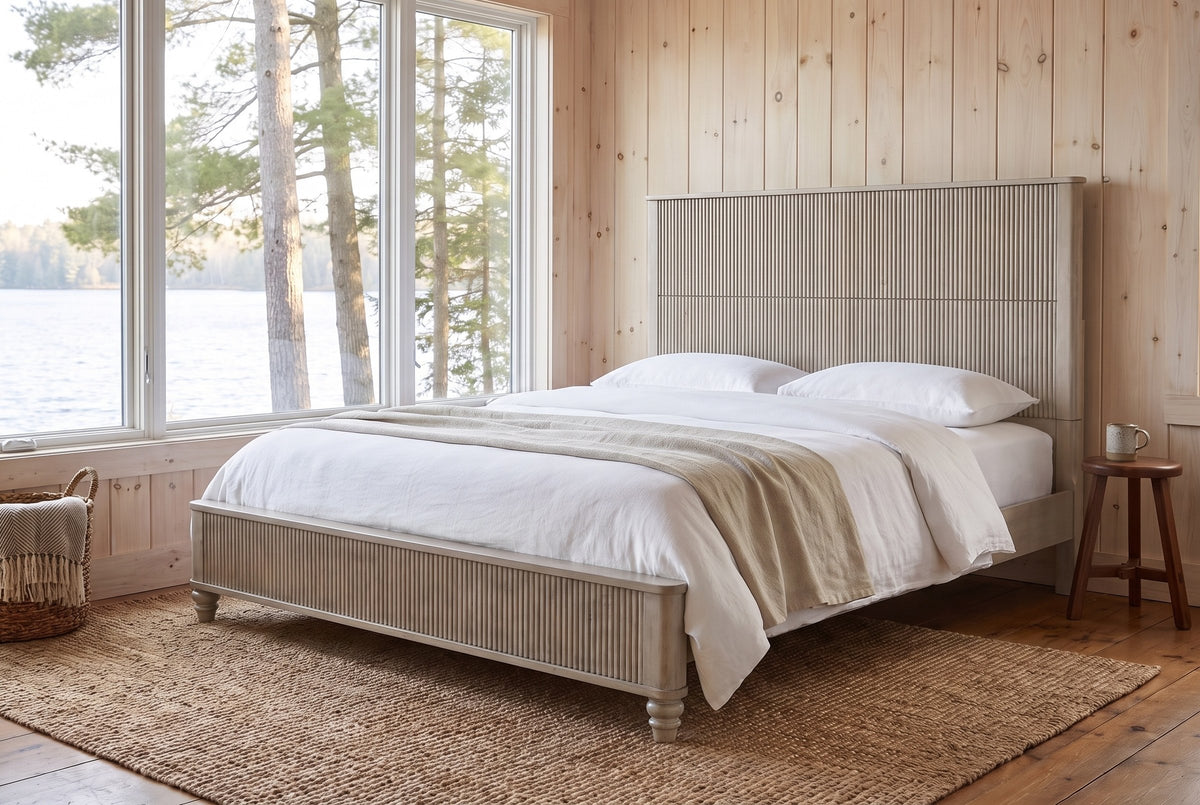 Volterra reeded bed in beige in a pine-panelled lakeside cottage bedroom with a jute rug