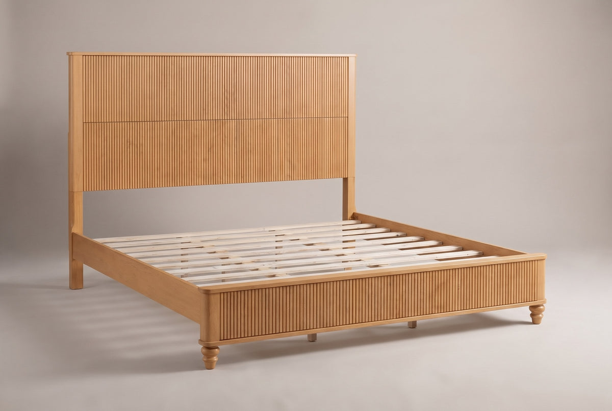 Volterra solid wood reeded bed in a natural honey finish, three-quarter view on a warm off-white studio backdrop