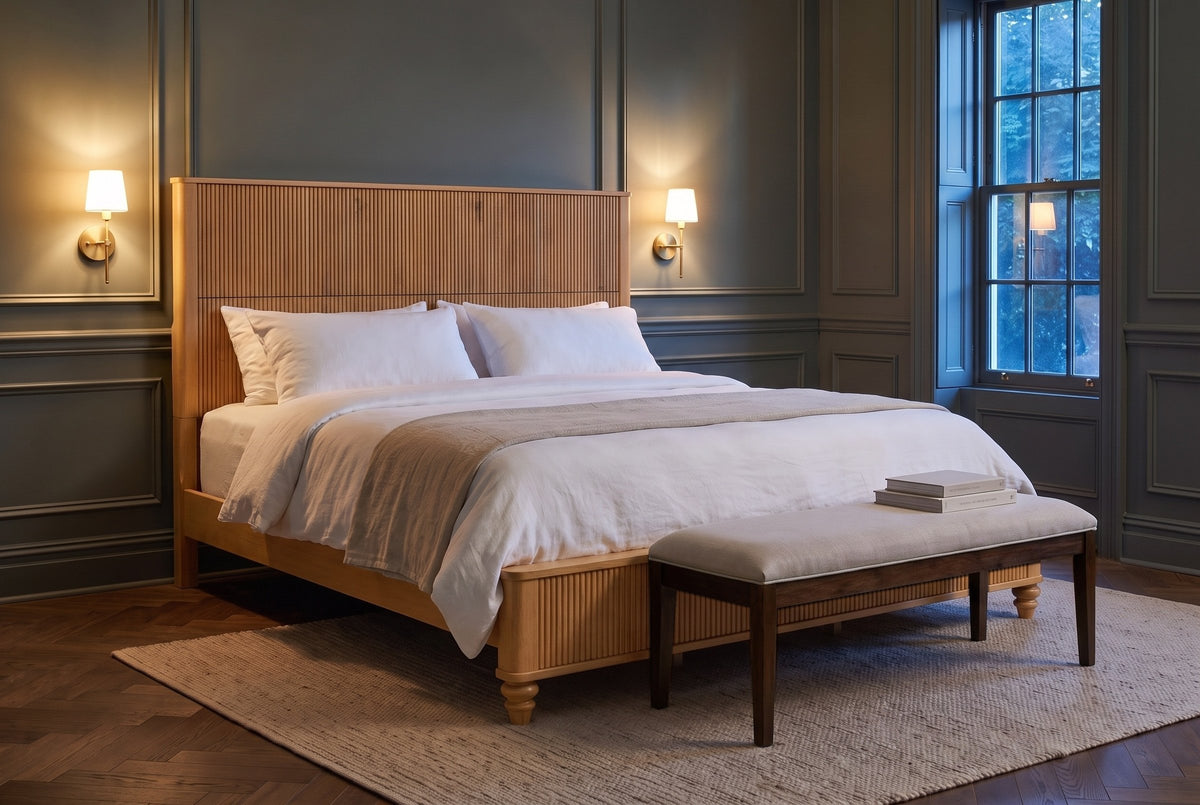 Volterra reeded bed in natural in a panelled bedroom at dusk with brass sconces lit and a linen bench at the foot