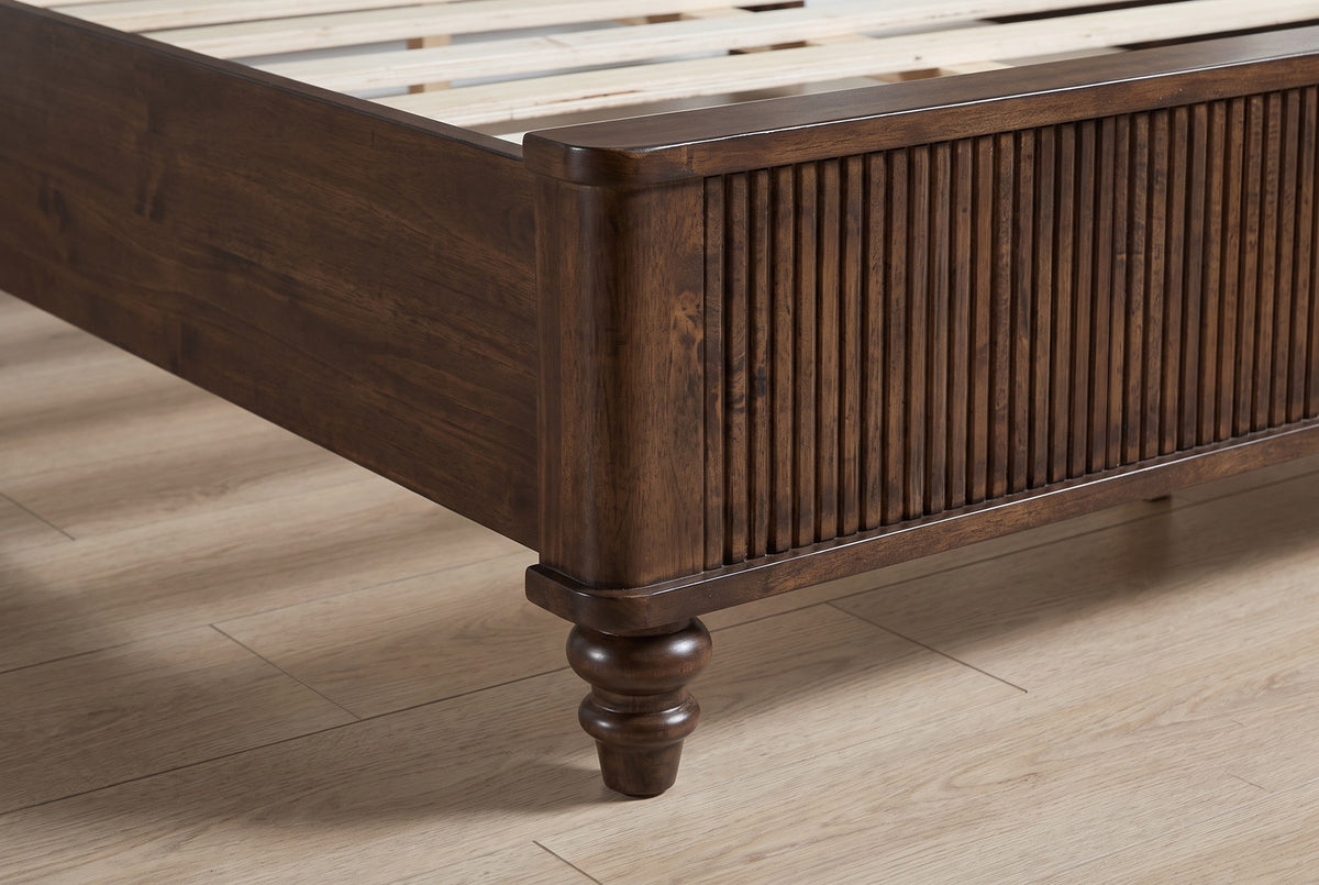 Close-up of the reeded footboard corner and a turned walnut bun foot on an oak floor