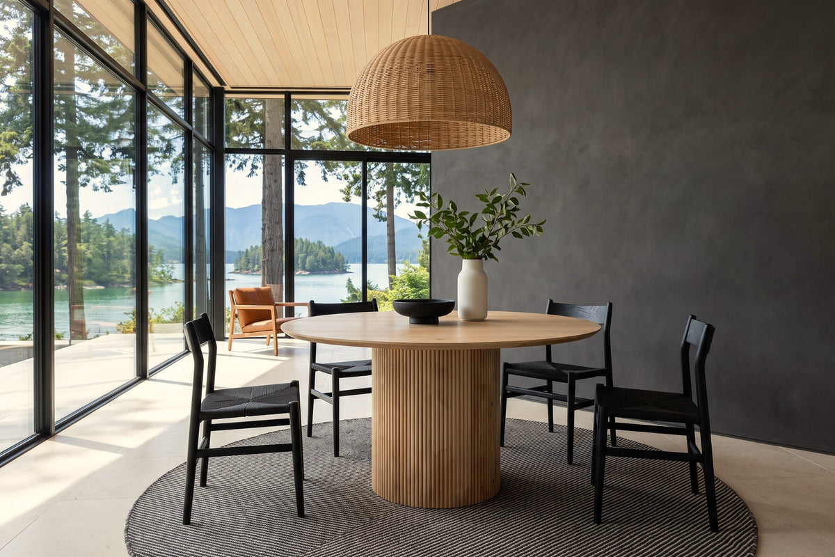 Zuccarello round dining table in a Pender Harbour house, with a charcoal plaster wall, a rattan dome pendant
