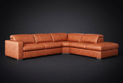 The Clara sectional against a dark studio backdrop, headrests down, the chaise on the right. Shown in distressed full-aniline leather, Tuscan Cognac, Right bumper.